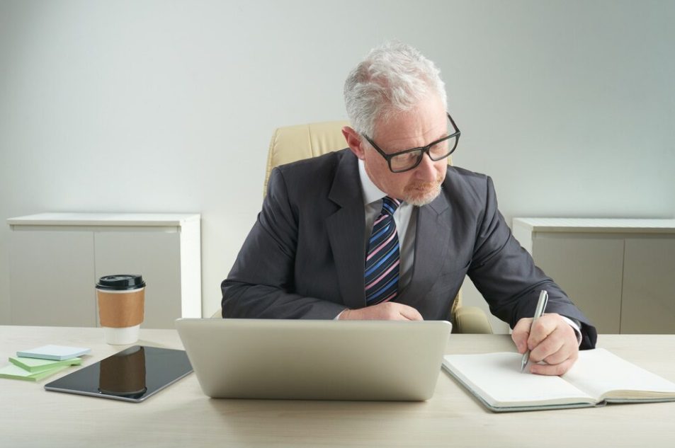 A man in suit and tie writing on paper.