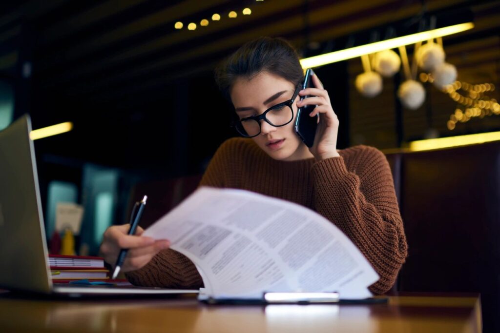 A woman is sitting at a table with papers and talking on the phone.